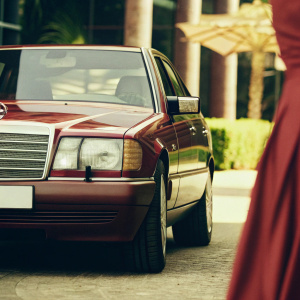 1994 Mercedes-Benz W124 E-Class, first Mercedes to enter Indian market. Promotional photo showcasing car's distinctive design, sleek front end, and balanced body. Architectural background with street elements.