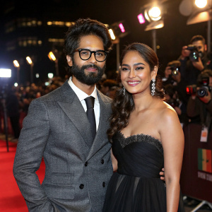 Shahid Kapoor and Mira Rajput attending a Bollywood film premiere. Shahid in grey suit with glasses, Mira in a black gown. Flashing cameras and crowds in the background.