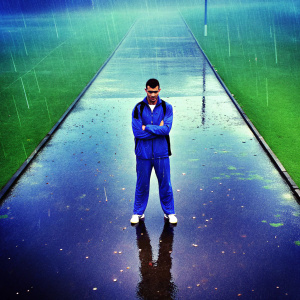 Granit Xhaka, midfielder in blue tracksuit, posing for interview at post-match press conference. Wet grass visible, raindrops falling
