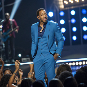 Ludacris, wearing a blue suit, on stage at BET Awards. Poses confidently in front of cheering crowd.