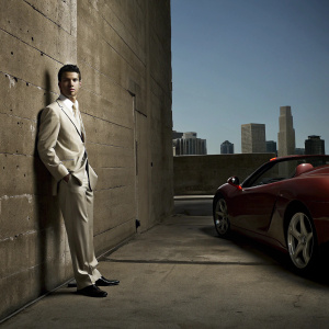 Cristiano Ronaldo standing beside a Ferrari, elegant attire. Blue sky backdrop, urban environment