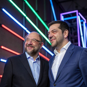 Martin Schulz and Alexis Tsipras, formally attired, during an EU summit. Neon light backdrop