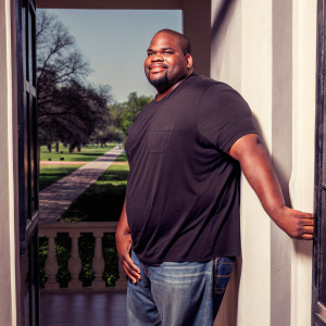 Vince Wilfork, former NFL player, posing in a casual black t-shirt and jeans. Bright, sunny park background, far depth of field, natural lighting, cheerful atmosphere, photo.