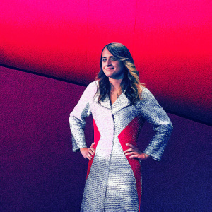 Caucasian actress Adele Haenel, late 20s, standing confidently. Long wavy brown hair, warm smile. White and red dress with textured front. Solid vibrant red background. Soft lighting highlights her facial features. Close-up portrait focused on upper body.