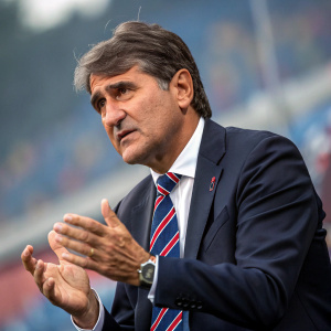 Luigi De Canio, coach of Catania, in a press conference. He wears a dark suit and striped tie. Serious expression, gesturing with hands.