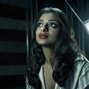 Radhika Apte in a glamorous close-up. Her makeup is striking with bold red lips and eye makeup. Professional photo with dramatic lighting. Dark background highlights her facial features.