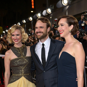January Jones, Will Forte, and Kristen Schaal attend a high-profile Hollywood party. They are standing against a backdrop of flashing cameras and excited fans.