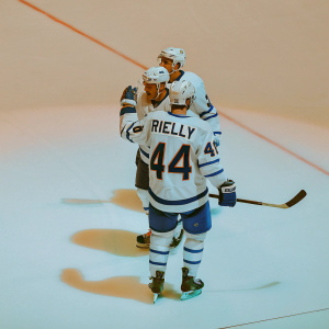 Toronto Maple Leafs players huddled on ice rink. White and navy uniforms. Intense focus on player with 'RIELLY 44' jersey. Crowd roars in background.
