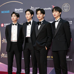 TNX, a korean boy band, poses for photos at the Seoul Music Awards. Formal black suits with bow ties. Backdrop features sponsor logos. Asian ethnicity, dark hair, upright pose.
