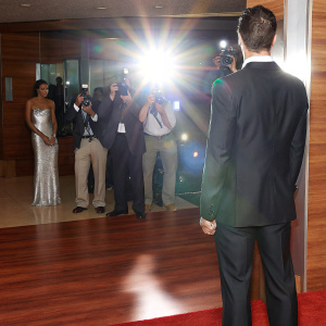 Cristiano Ronaldo in a sleek black suit, center stage at a glitzy award show. Spotlight illuminating him, flashing cameras.