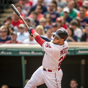 Roberto Perez, baseball player for the Cleveland Indians, mid-swing in a white jersey with red trim. Crowd in the background
