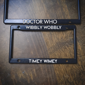 License plate frame featuring 'Doctor Who' quote 'Wibbly Wobbly Timey Wimey'. Sleek black finish with white text. Sturdy design.