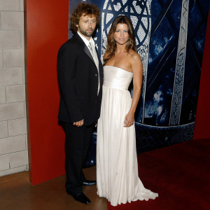 Michael Sheen and Rhona Mitra at 'Underworld: Rise of the Lycans' premiere. Sheen, with curly hair and a beard, in a sleek black suit. Rhona in a flowing white strapless gown. Stylized graphic backdrop with Gothic themes