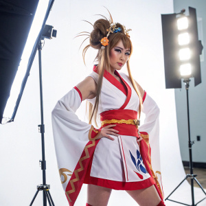 Female character from anime series Ikkitousen. Standing in a powerful pose, elaborate hairstyle, and traditional yet fashionable attire. Brightly lit studio setting