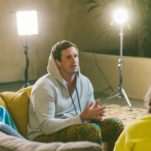 Ryan Lochte, wearing a casual hoodie, sitting on a couch. Q&A session. Bright studio lights