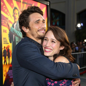 James Franco and Marla Sokoloff hugging during a premiere event. Dynamic movie poster behind them with bright colors