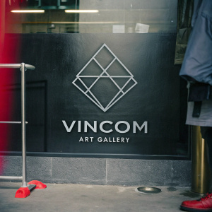 A sleek logo for the Vincom Art Gallery. It features a bold diamond shape with interconnected lines. Modern sans-serif font text is placed beneath the graphic, all on a black backdrop. The design highlights minimalism and contemporary art.