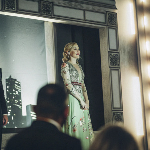 AnnaSophia Robb, in a green dress with intricate floral designs, stands at the Gotham Awards ceremony. Dark, dramatic backdrop with Gotham skyline