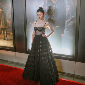 Jing Tian at a film festival premiere, standing confidently in front of a movie poster. She is wearing a black, layered, strapless gown with intricate ruffles and a sheer overlay. Asian female with a bun hairstyle. High-resolution photo.