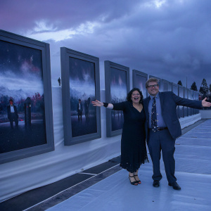 Andy Daly and Carri Levinson at a movie premiere. They are smiling broadly, posing against a backdrop filled with movie posters.