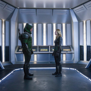 Stephen Amell as Oliver Queen and Emily Bett Rickards as Felicity Smoak. High-tech room with glowing panels. Stark white walls