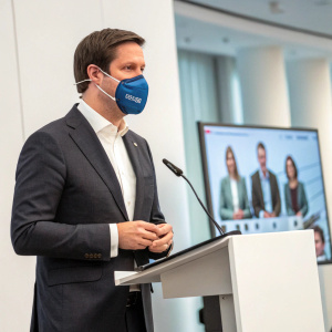 Manuel Hagel, CDU leader, addressing virtual party members. Wearing a dark grey suit and white shirt. Wears a blue mask with an earpiece.