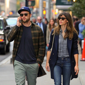 Justin Timberlake and Jessica Biel walking down a bustling New York City street. Justin Timberlake has his phone to his ear, adjusting his sunglasses. Jessica Biel listens attentively, both dressed casually.