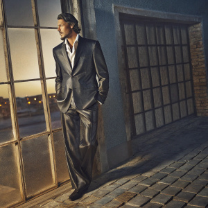 Eric Balfour, sharp jawline and well-groomed facial hair, in a sleek black suit and crisp white shirt. Golden hour lighting, blurred cityscape background.