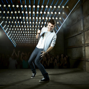 Nathan Sykes, performing energetic stage act. Vibrant lighting design, colorful bulbs, audience in blurred background