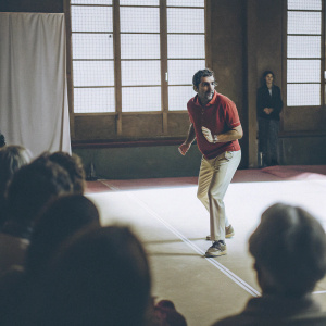 Pablo Larrazabal, in a red polo shirt and khaki pants, running on a tennis court. A crowd watches from the sidelines.