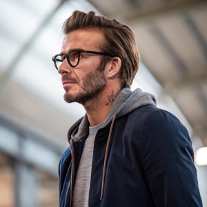 David Beckham, close-up shot. Soccer player, wearing glasses, casual attire. Indoor setting, blurred background