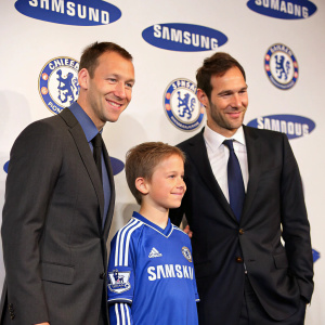 John Terry, Petr Cech, and a young Chelsea mascot in formal wear. They are at a press conference with a Samsung-branded backdrop.