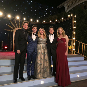 The cast of 'The Real O'Neals' at a glamorous award show. Dressed in formal attire, posing together on a stage with flashing lights.