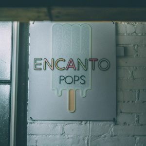 The Encanto Pops logo showcases a sleek popsicle design. Dominated by pastel tones, it features 'ENCANTO' above and 'POPS' below. Clean lines and minimalist style with dripping effect on a crisp white backdrop.