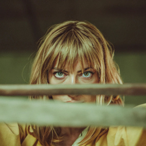 Close-up of Beatrix Kiddo, blonde hair, intense look, shot against a dark backdrop.