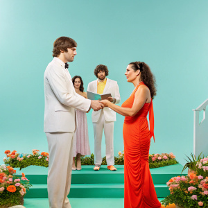 Ashton Kutcher and Demi Moore in a candid photo from their wedding day. He is dressed in a classic tuxedo, she in an elegant, form-fitting wedding gown. The setting is their garden ceremony with friends and family in the background.