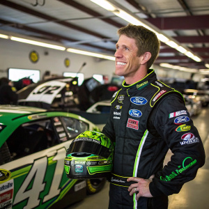 Carl Edwards, nascar driver, smiling in racing gear. Garage setting. Sponsor logos visible