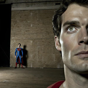 Photograph showcasing Henry Cavill dressed as Superman. Focused on facial features. Sharp jawline, prominent cheekbones, and striking eyes. Wearing iconic red and blue suit. Against a simple black backdrop.