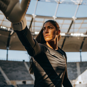 Hope Solo, goalkeeper, in a Nike sponsored jersey. Dynamic pose in an empty stadium. Blue sky background, high-resolution photo