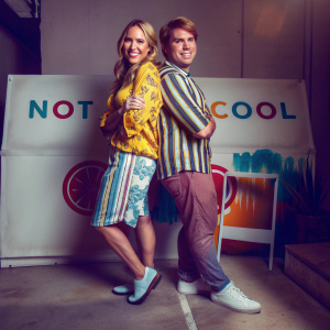Lisa Schwartz and Shane Dawson, smiling and relaxed, in a promotional shoot. They stand against a bold, graphic white backdrop featuring Not Cool logos and other designs.
