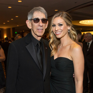 Candid shot of Richard Belzer and Harlee McBride at a charity gala. Formal attire, indoor lighting, crowd in background.