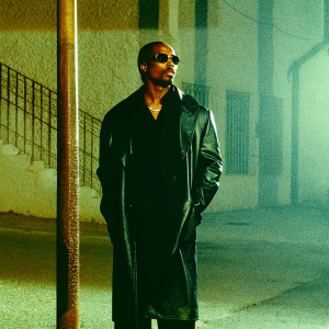 Tupac Shakur, in a black leather jacket and dark shades, standing in a dimly lit alley.