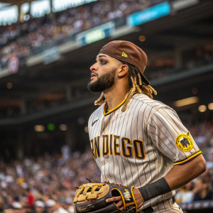 Fernando Tatis Jr., donning his San Diego Padres uniform, in the midst of a bustling stadium crowd. Intense focus, brown cap, dreadlocks, and makeup enhancing his features. Wearing a baseball glove.