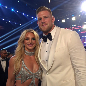 Britney Spears and J. J. Watt at a glitzy award show. Britney in a sparkly outfit, J. J. in a tuxedo. Vivid stage lights