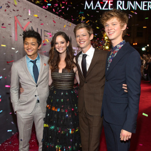 Celebrity photo shoot: Ki Hong Lee, Kaya Scodelario, Thomas Brodie-Sangster, and an unknown actor. At the premiere of Maze Runner. The backdrop is a chaotic mix of colorful confetti and sponsor logos.