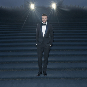 David Beckham in sharp suit, posed at glitzy gala. Clean-cut beard, styled hair. Formal attire stands out against bright, sunny backdrop.