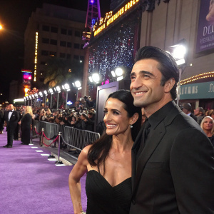 Gilles Marini and Carole Marini at a glamorous movie premiere. Purple carpet, bustling crowd, flashing cameras, cheerful atmosphere