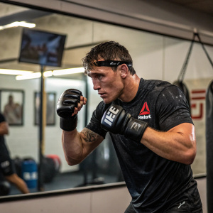 Darren Till, in a gym, wearing boxing gloves and UFC shirt, intense workout session