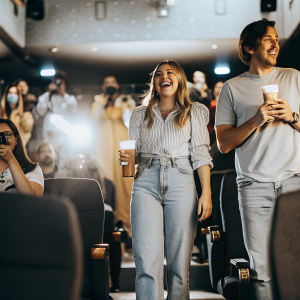 Chloe Grace Moretz and Christopher Mintz-Plasse at a lively movie premiere. Both are dressed in casual outfits. Chloe in a casual blouse and jeans, Christopher in a t-shirt and denim. The venue is filled with fans and flashing cameras.