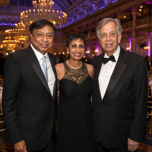Formal attire-clad Lakshmi Mittal, Usha Mittal, and Bob Roth at a corporate gala. Lavish ballroom setting.